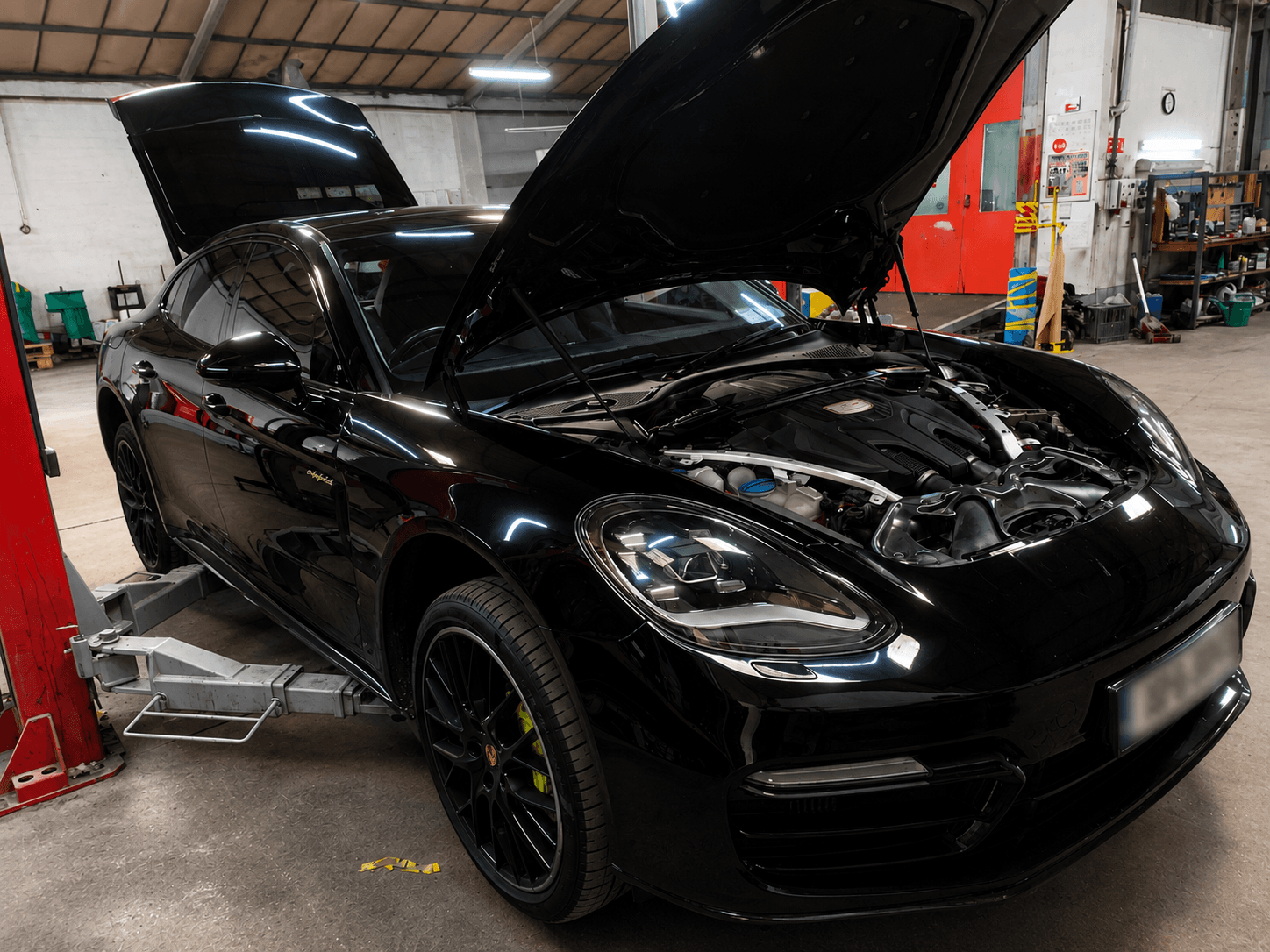 Black Porsche Panamera with its bonnet open inside the workshop