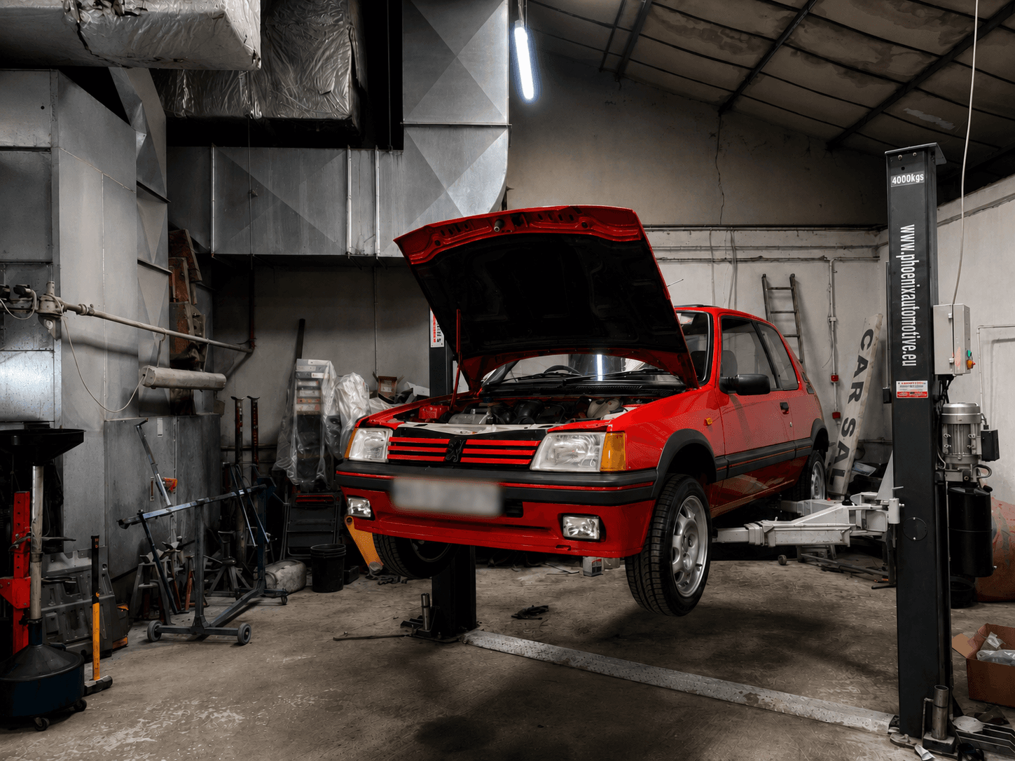 Red Peugeot 205 GTI with its bonnet open inside a workshop
