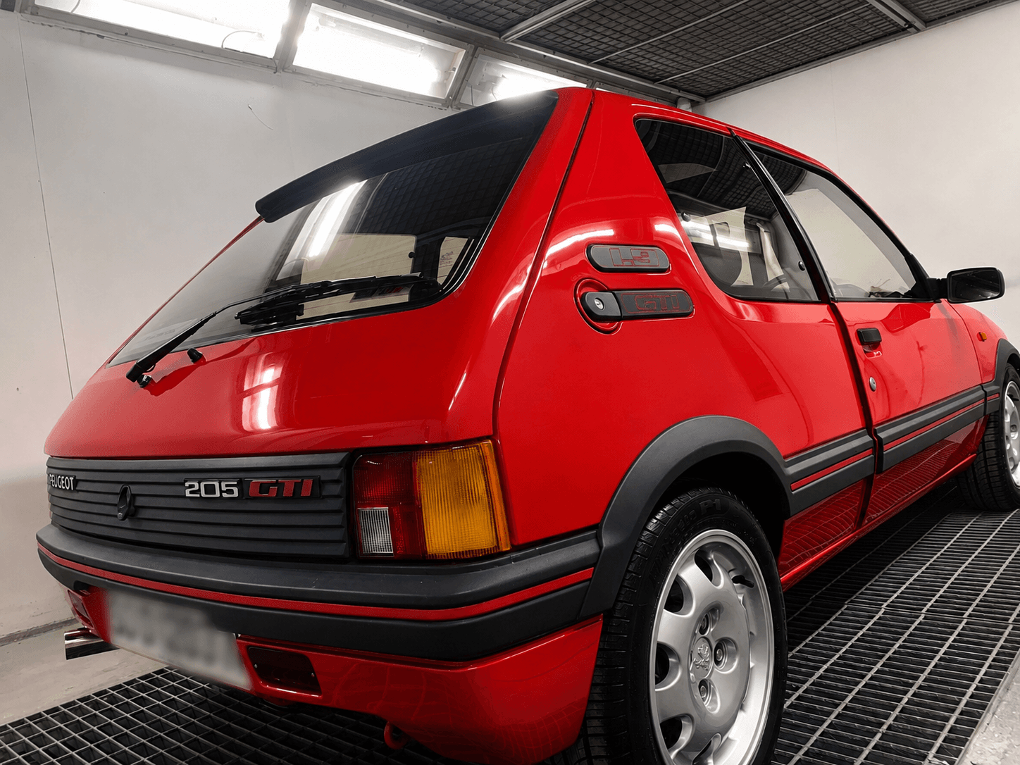 Red Peugeot 205 GTI viewed from the rear inside a paint booth